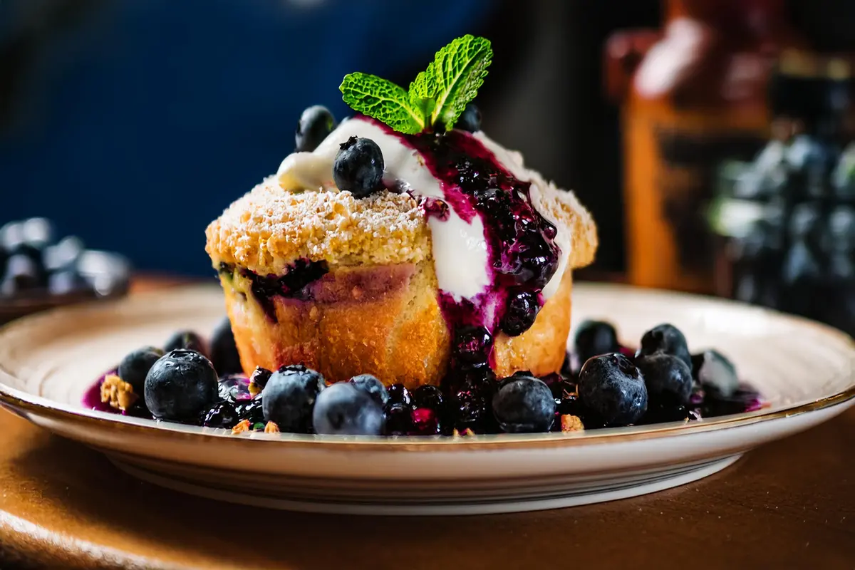 Freshly baked Bisquick blueberry muffins on a plate, surrounded by scattered blueberries.