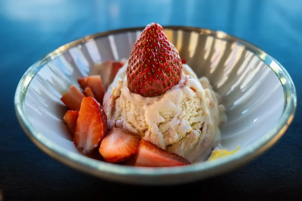 A bowl of strawberry shortcake ice cream with fresh strawberries and shortcake crumbles on top.